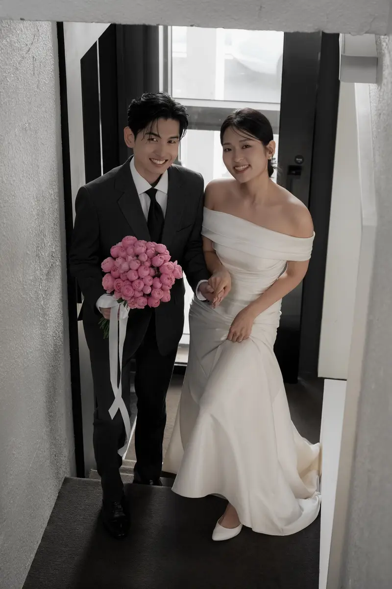 계단을 함께 오르며 돌아보는 두 사람. 신랑이 분홍 부케를 들었다